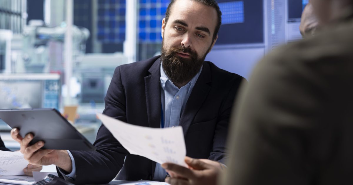 Investors in factory ensuring adherence to industry regulations, looking over paperwork documents. Shareholders ensure following of safety standards before investing, checking documentation files